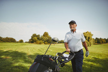 Smiling senior man pushing his golf clubs along a fairway