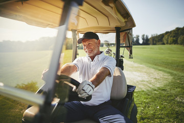 Smiling senior man driving his golf cart on a fairway