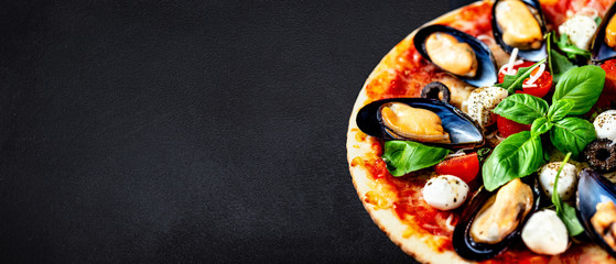 Seafood Italian Pizza on black stone background, top view. Pizza with Mussels, Tomatoes, Basil leaf and Mozzarella Cheese close up. Copy space
