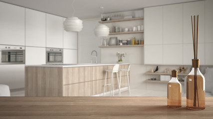 Wooden table top or shelf with aromatic sticks bottles over blurred contemporary modern wooden kitchen with shelves and cabinets, white architecture interior design