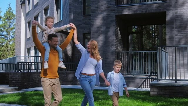 Clean ecology luxury residential property exterior and family portrait. Unity with nature summer scene. Husband and wife with kids walking at backyard, smiling and laughing, entertainment concept