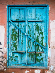 Old blue closed window with shutters. Ruined wall of an old house