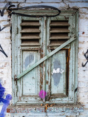 Old gray closed window with shutters. Ruined wall of an old house