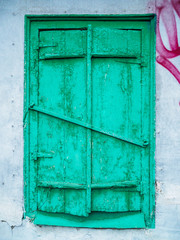 Old green closed window with shutters. Ruined wall of an old house