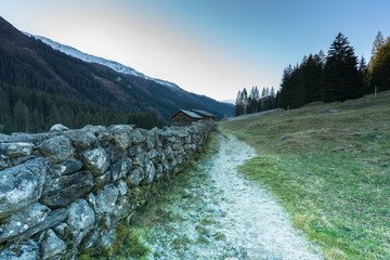 Fototapeta premium mountain landscape and valley with forest and snow-capped mountain peaks and an old rock wall with wooden huts and chalets behind