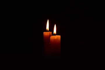 Yellow light candle burning brightly in the black background.