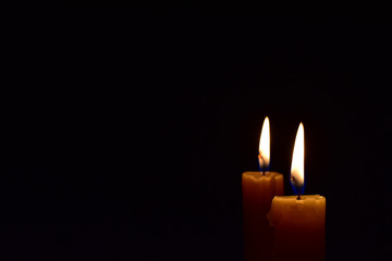 Yellow light candle burning brightly in the black background.