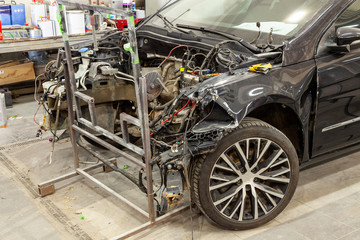 The black car after a serious accident with a completely broken front of the body without an engine with broken glass that is awaiting repair in a workshop for body paint of vehicles