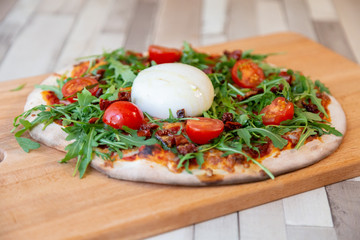 a pizza on a wooden board with cherry tomatoes, arugula, and cheese