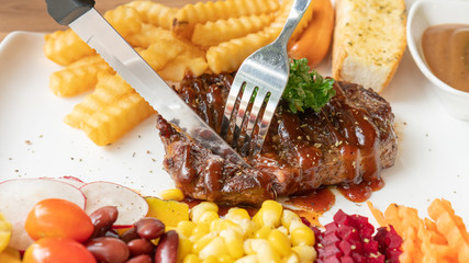 Beefsteak, French fries, and vegetable on a white plate.