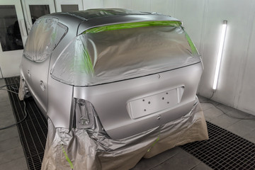 Full painting of the car in the back of a silver hatchback window and the wheels of which are covered with paper from hitting the paint in a special camera for body repair of vehicles in the workshop