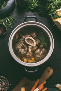 Broth of beef meat shin with bone in cooking pot on dark kitchen table background with ingredients for soup, top view. Meat broth or stock. Clean low-calorie food and eating concept