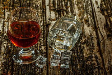 A glass of whiskey with ice or brandy and a square carafe on an old woody background. Whiskey with ice in a glass. Selective focus.
