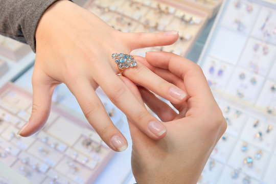 A girl in a jewelry store tries on her finger a gold ring with diamonds on the background of a shop window. Buying and shopping. Woman jeweler.