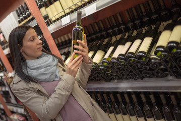 Fototapeta na wymiar Woman choosing wine at the supermarket. Consumerism concept.