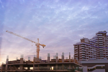 Fototapeta na wymiar construction of high-rise buildings with yellow tower crane at sunset and dark blue clouds