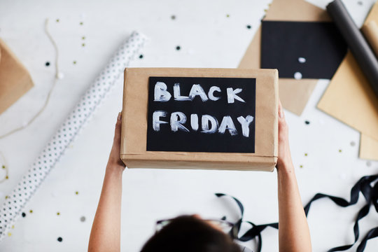 Directly above view of unrecognizable woman holding gift box with painted  lettering Black Friday over table with wrapping paper