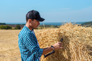 A young farmer in a field with a tablet and a magnifying glass evaluates the hay harvest