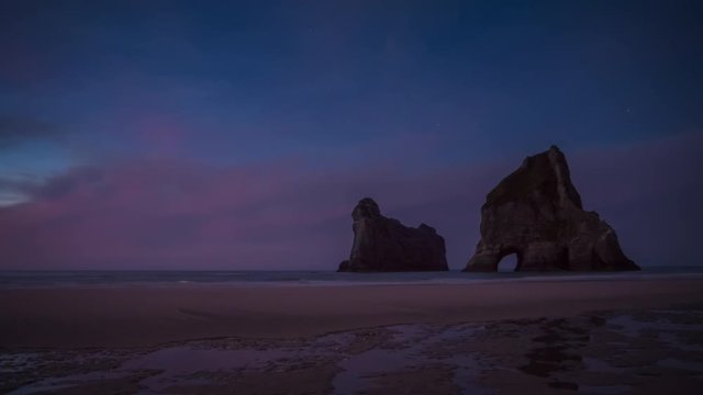 Timelapse video of evening on a beautiful empty beach with natural archway in massive rocks off the coast. Wharariki Beach, New Zealand.