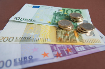 Banknotes of five hundred, two hundred, one hundred euros and one Euro coins on a brown background