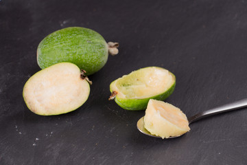 Cut fruit of the mature feijoa on a dark slate background. Pulp fruit on the bark spoon