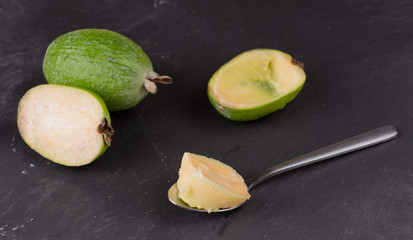 Cut fruit of the mature feijoa on a dark slate background. Pulp fruit on the bark spoon