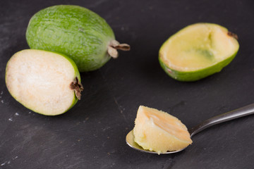 Cut fruit of the mature feijoa on a dark slate background. Pulp fruit on the bark spoon