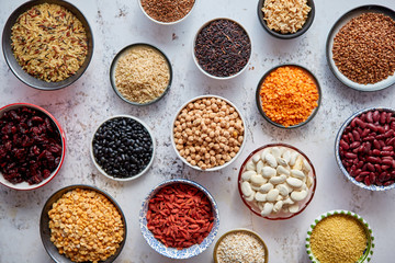 Organic superfood assortment in bowls. With raw peas, beans, wild rice, lentil, Goji berries, cranberry, couscous, linseeds on white rusty background. Above view.