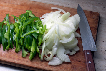 Green bell pepper, white onion and a knife on a cutting board. The vegetables are fresh and recently sliced. Concept of healthy eating and lifestyle.