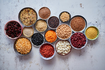 Organic superfood assortment in bowls. With raw peas, beans, wild rice, lentil, Goji berries, cranberry, couscous, linseeds on white rusty background. Above view.