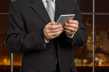 Businessman holding smartphone close up. Mature man in formal wear using his phone on evening office background. People, business, technology.