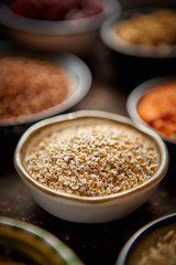 Raw groats seeds in ceramic bowl. Composition of superfoods in background. Placed on dark rusty table. Selective focus.