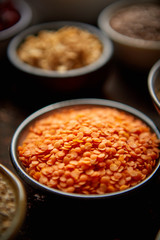 Raw lentil seeds in ceramic bowl. Composition of superfoods in background. Placed on dark rusty table. Selective focus.