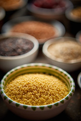 Raw couscous seeds in ceramic bowl. Composition of superfoods in background. Placed on dark rusty...