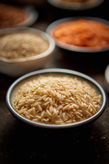 Raw jasmine rice seeds in ceramic bowl. Composition of superfoods in background. Placed on dark rusty table. Selective focus.