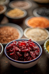 Dry cranberries in ceramic bowl. Composition of superfoods in background. Placed on dark rusty table. Selective focus.