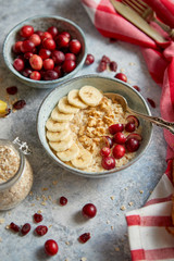Ceramic bowl of oatmeal porridge with banana, fresh cranberries and walnuts on stone table top view in flat lay style. Healthy breakfast and diet food.