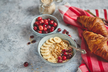 Ceramic bowl of oatmeal porridge with banana, fresh cranberries and walnuts on stone table top view in flat lay style. Healthy breakfast and diet food.