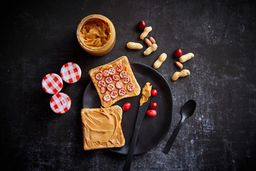 Obraz na płótnie Canvas Toasts bread with homemade peanut butter served with fresh slices of cranberries. With jam jars and peanuts on side. Top view with copy space
