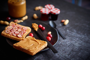 Toasts bread with homemade peanut butter served with fresh slices of cranberries. With jam jars and peanuts on side. Top view with copy space