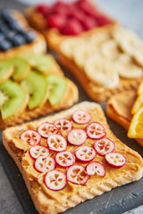 Six toasts with peanut butter, fresh fruits on a grey slate, stone or concrete background. Top view with copy space.