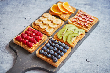 Healthy breakfast toasts. Wholegrain bread slices with peanut butter and various fruits. Served on grey cutting board. Top view, grey stone background. Dieting concept