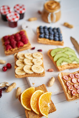 Assortment of healthy fresh breakfast toasts. Bread slices with peanut butter and various fruits and ingredients on side. Placed on white wooden table. Top view, with copy space. Selective focus