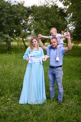 Naklejka na ściany i meble Happy family together in summer garden/park. Mother holding inscription `family` .Father giving piggyback ride to son. Outdoor photo