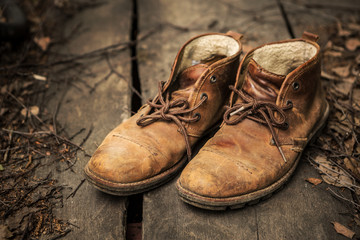 A pair of nubuck hiking boots on wooden floor with dead leaves ang twigs.