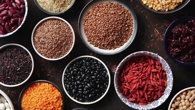 Various superfoods in smal bowls on dark rusty background. Superfood as rice, lentil, beans, peas, goji, flaxseed, buckwheat, couscous, chickpeas Top view Flat lay