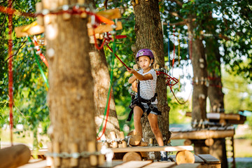 girl with climbing gear in an adventure park are engaged in rock climbing or pass obstacles on the rope road.