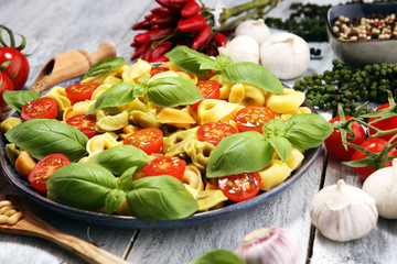 pasta. tricolor tortellini pasta salad with tomatoes and onions on wood table background.