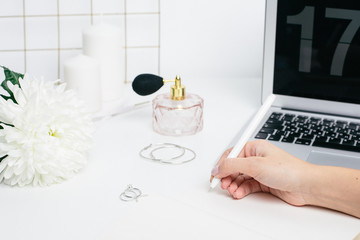 Female hands making notes in a notepad on a white table with a laptop keyboard