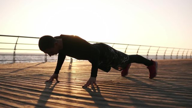 Picture of a young sportsman doing push ups outdoors on the wooden froor in front the sea or ocean. Fitness and exercising on the seaside. Sport, recreation, boxing lifestyle concept